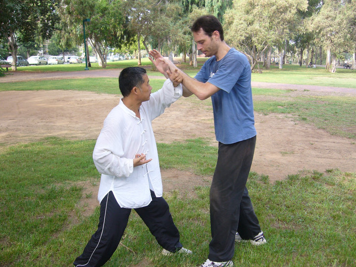 Master Zhou, demonstrating application with his Israeli student, Etai. During this particular moment, Zhou was showing how proper alignment and structure, as developed through Zhan Zhuang training, can make it easy for a small person to resist a much larger individual. Zhou is roughly 5'6 in height, and Etai is 6'4. HaYarkon Park, Tel-Aviv, Israel, August 2010.